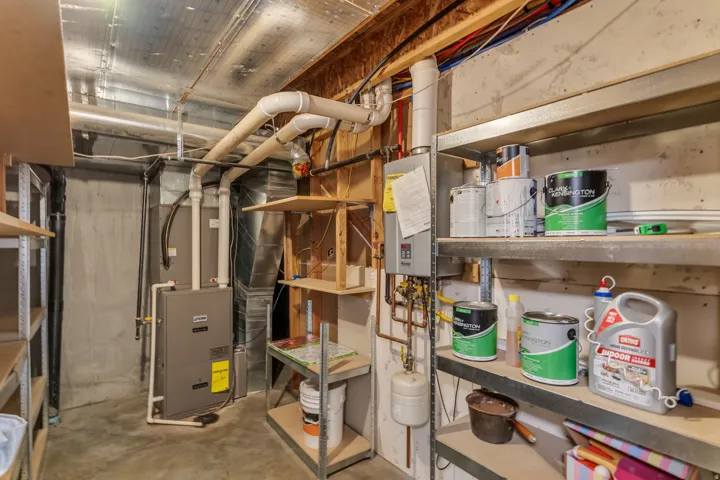 Concrete flooring with a furnace, exposed ceiling joists, and extensive piping