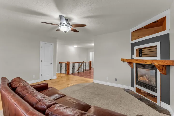 Built-in fireplace with a wooden mantel, integrated shelving with accent lighting, and a ceiling fan