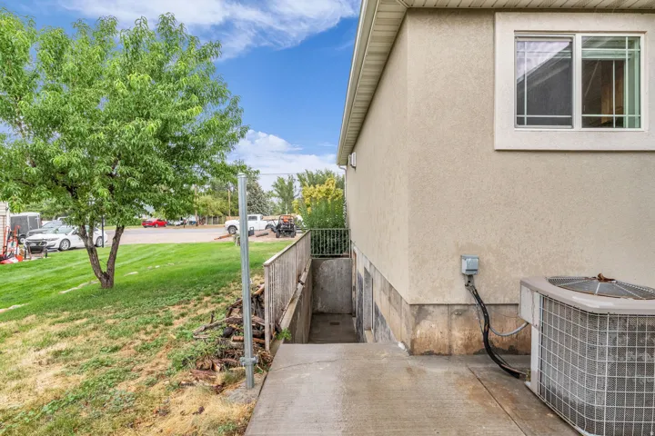 Exterior stucco finish, visible window with white trim, concrete pathway, mature tree, and a sloped grass lawn