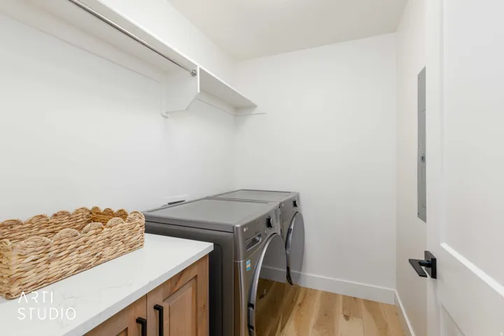 Laundry area featuring a wood-finish floor, white walls, and a built-in white shelf with a hanging rod