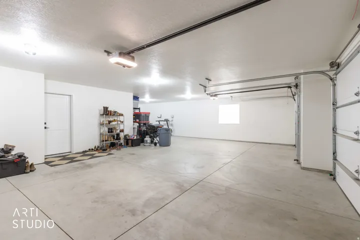 Spacious garage with exposed overhead garage door mechanisms, concrete flooring, and multiple overhead light fixtures