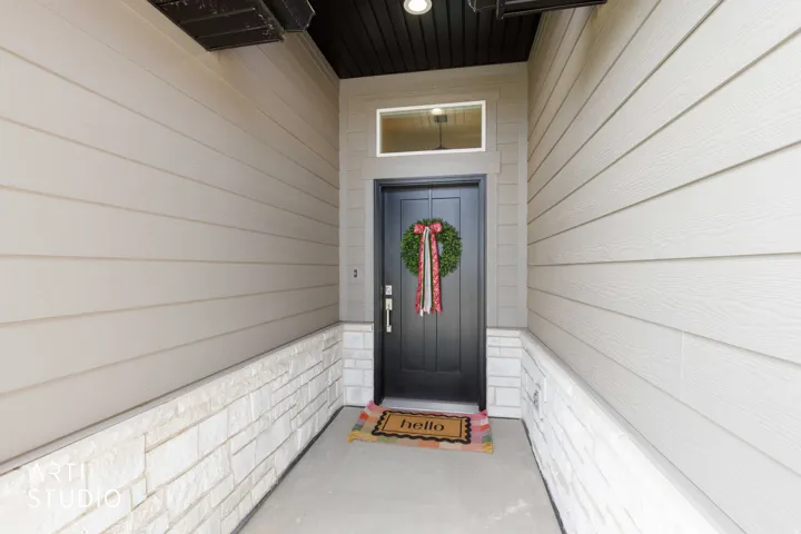 Gray paneled entry door with transom window, complemented by light-colored siding and a stacked stone accent wall