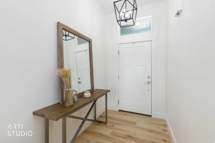 Entryway featuring wood-finish flooring, a white paneled door with transom window, and a geometric pendant light fixture