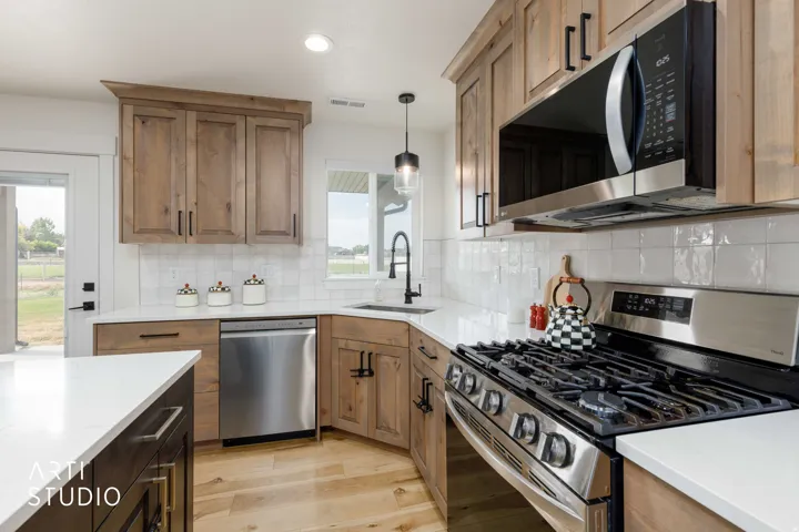 Stainless steel appliances, wood-finish cabinetry, white countertops, tile backsplash, and wood-finish flooring