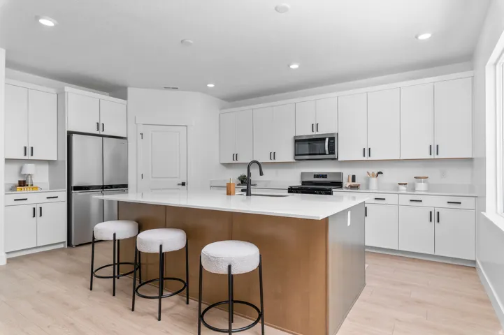 Modern kitchen featuring light wood-finish flooring, white cabinetry with black hardware, stainless steel appliances, white countertops, and a central island with an integrated sink