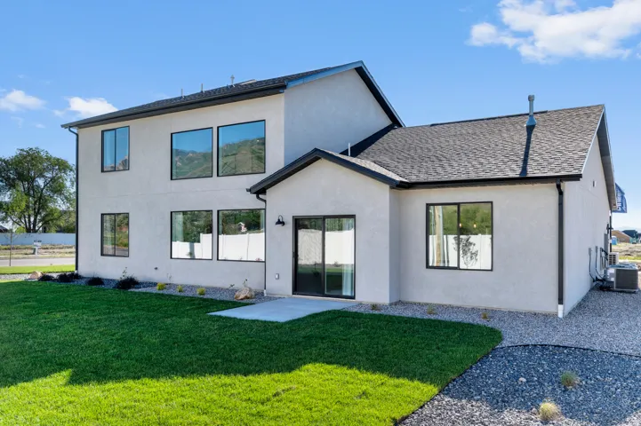 Contemporary stucco exterior with a dark shingle roof, black-framed windows, and a manicured lawn