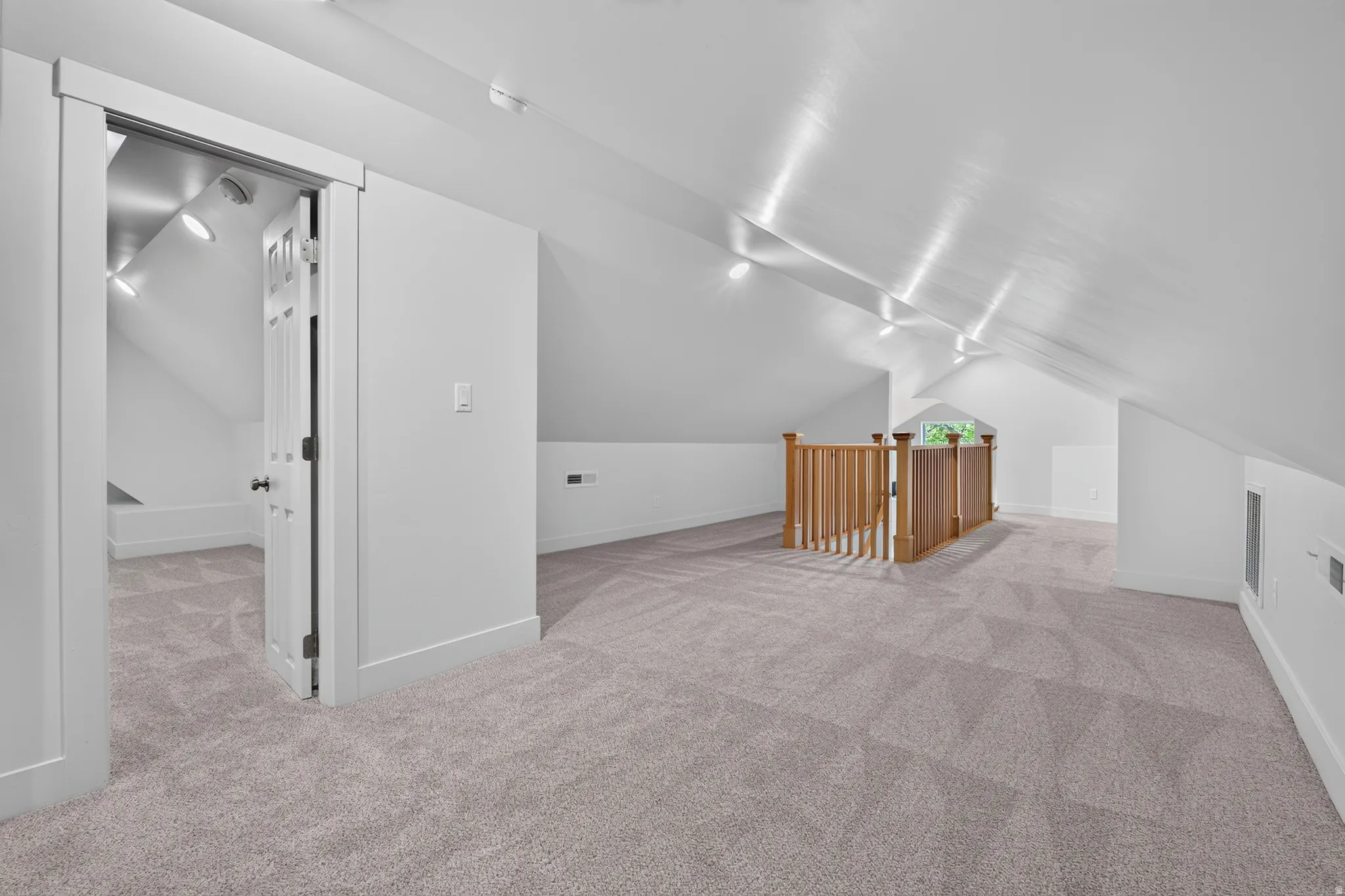 Expansive carpeted loft area with sloped ceilings, recessed lighting, and a natural wood-finish railing