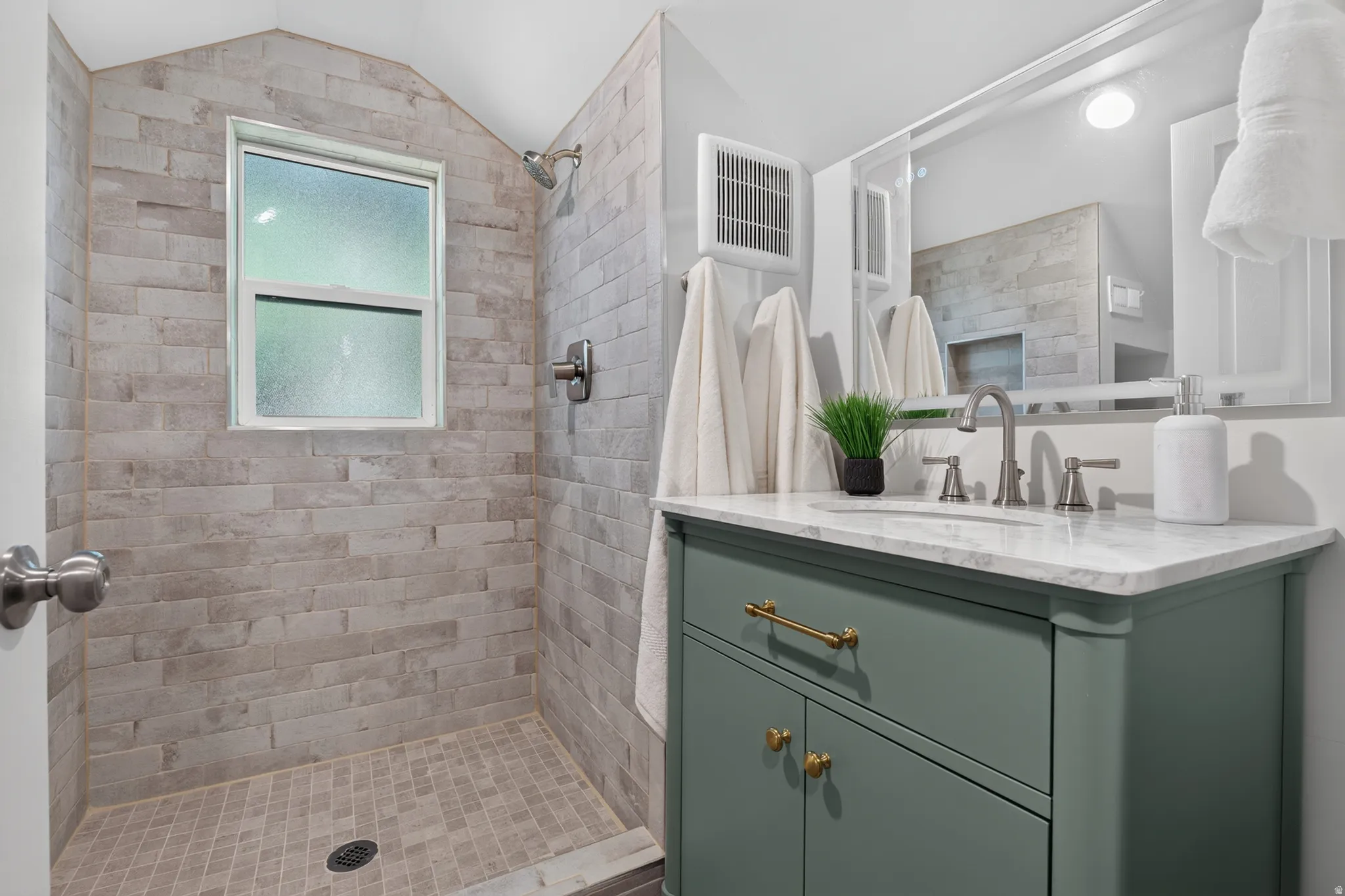 Tiled shower with a window, single vanity with a stone countertop, under-mount sink, and a framed mirror