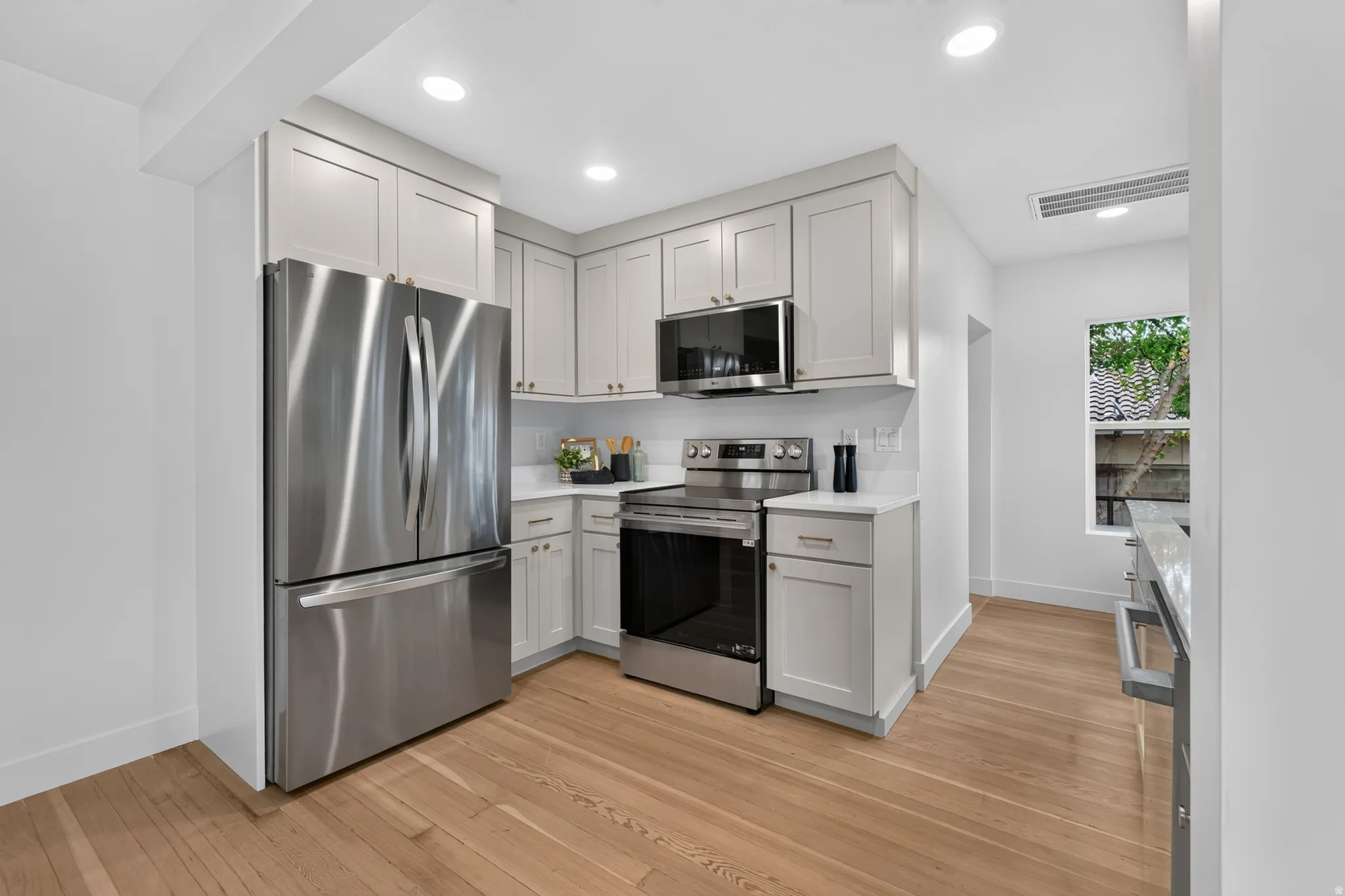 Modern kitchen featuring stainless steel appliances, light-toned cabinetry, a white tile backsplash, and light wood-finish flooring