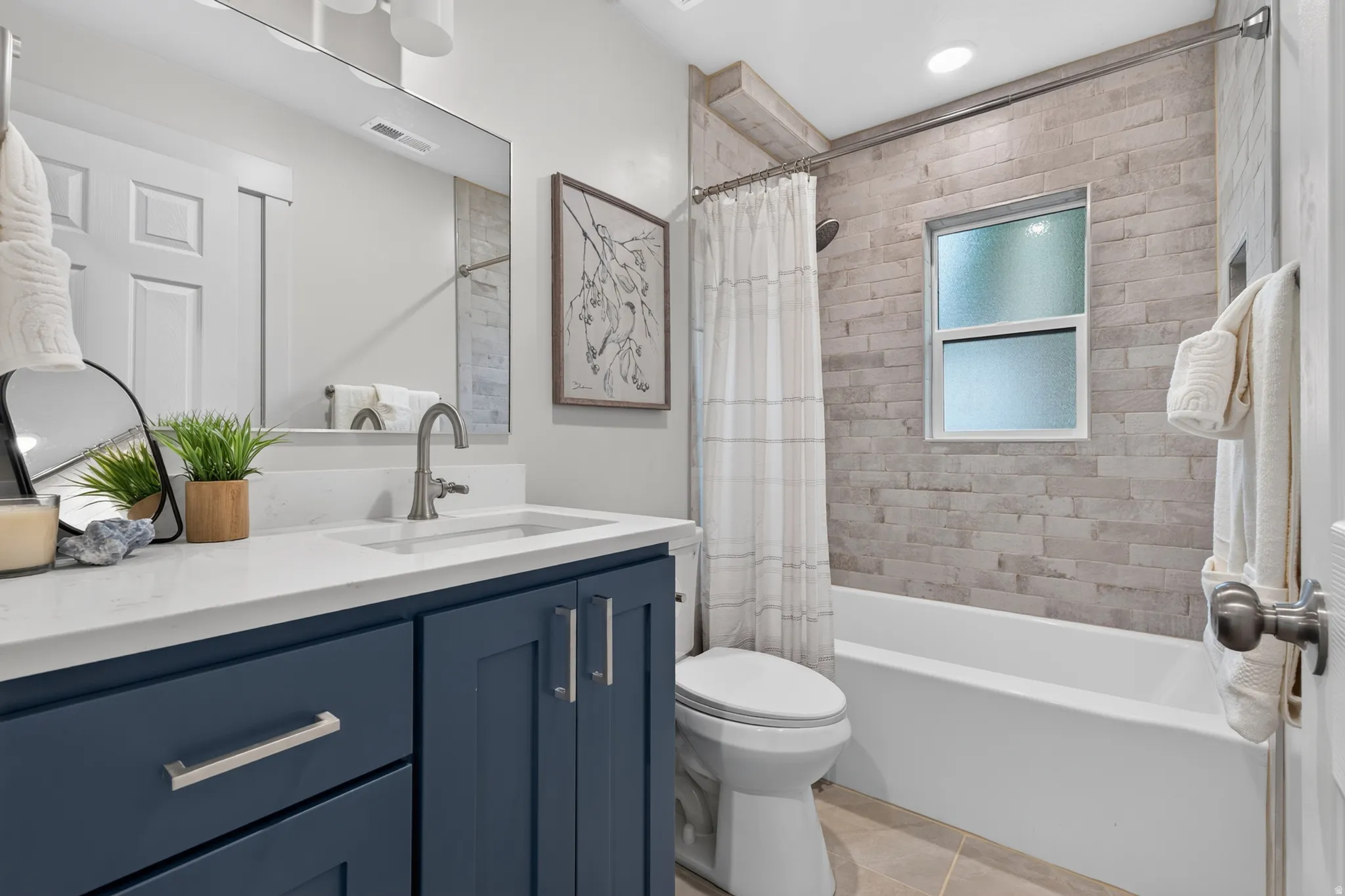 White vanity countertop with an undermount sink and brushed nickel faucet, blue cabinetry with brushed nickel hardware, and a tub with stacked stone-look tile surround