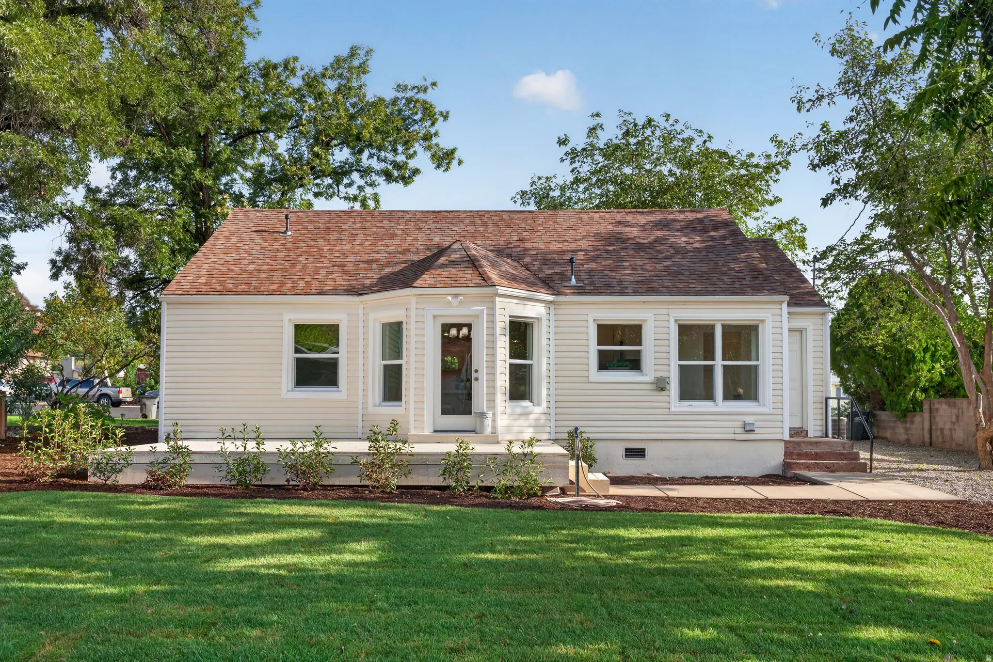 Manicured lawn, elevated deck, bay window, light-toned siding, and a brown shingle roof