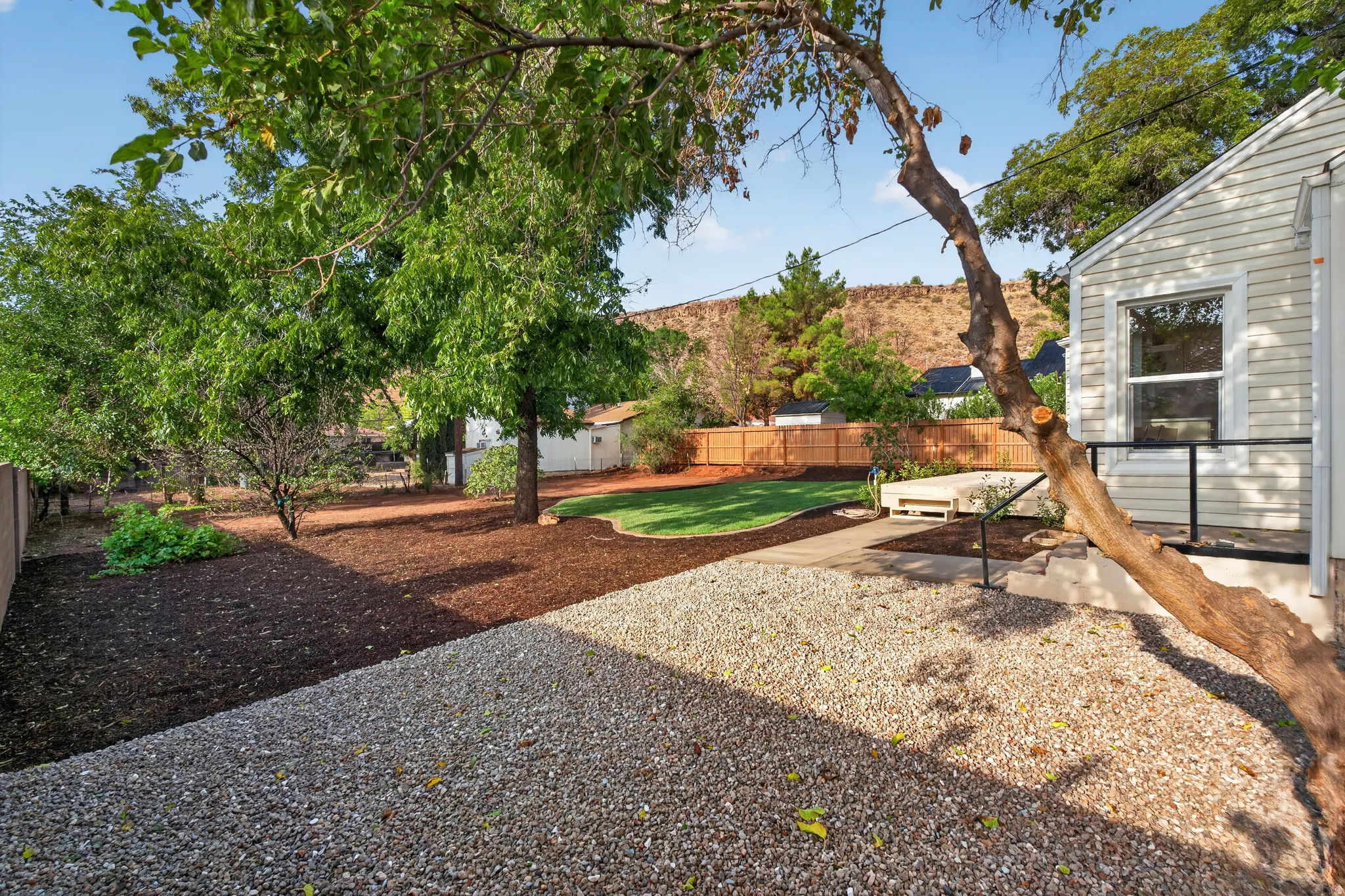 Expansive backyard featuring a manicured lawn, established trees, a fenced perimeter, and a gravel-covered area