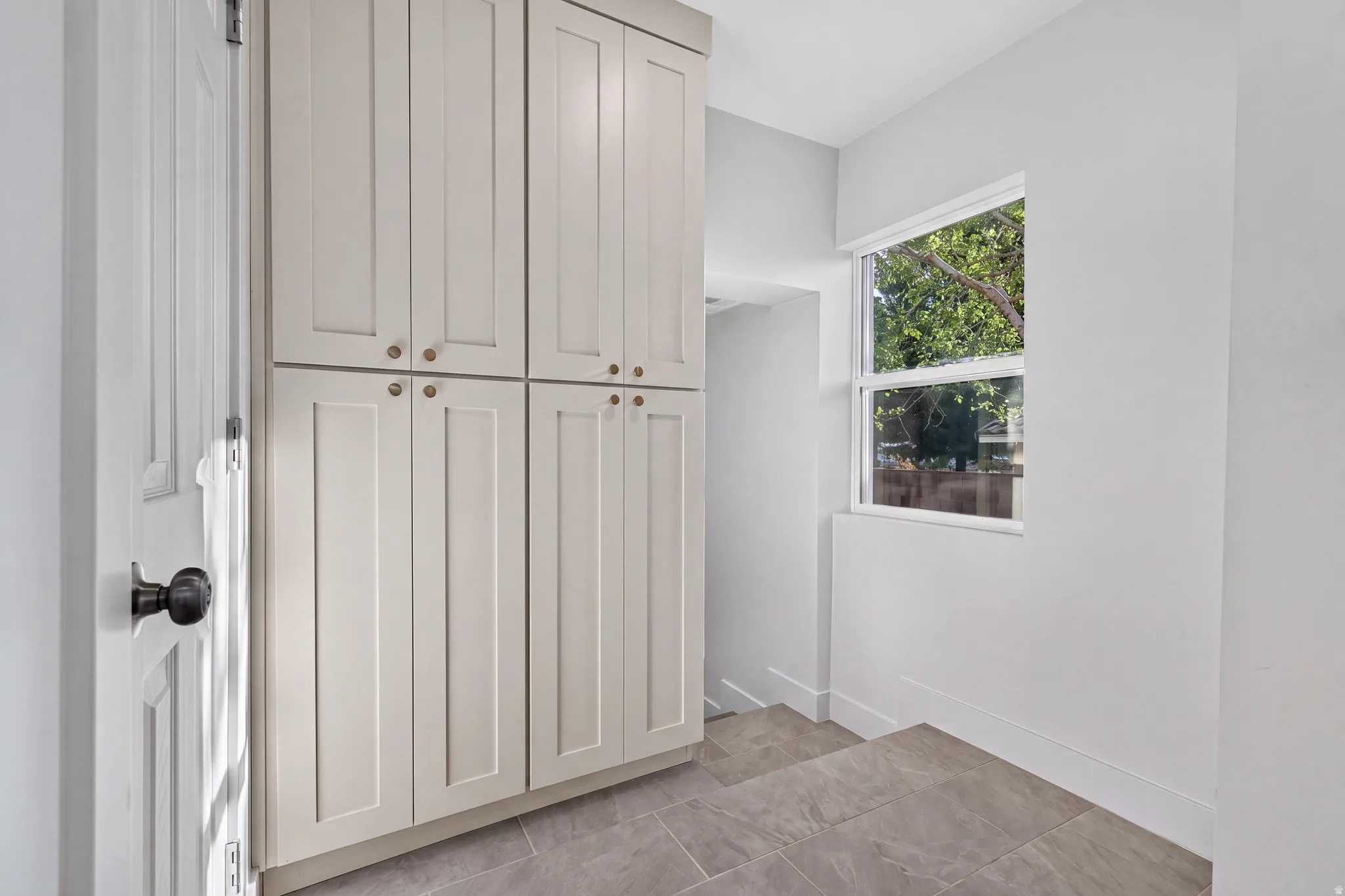 Full-height built-in cabinetry with bronze hardware, a single window, and large format floor tiling