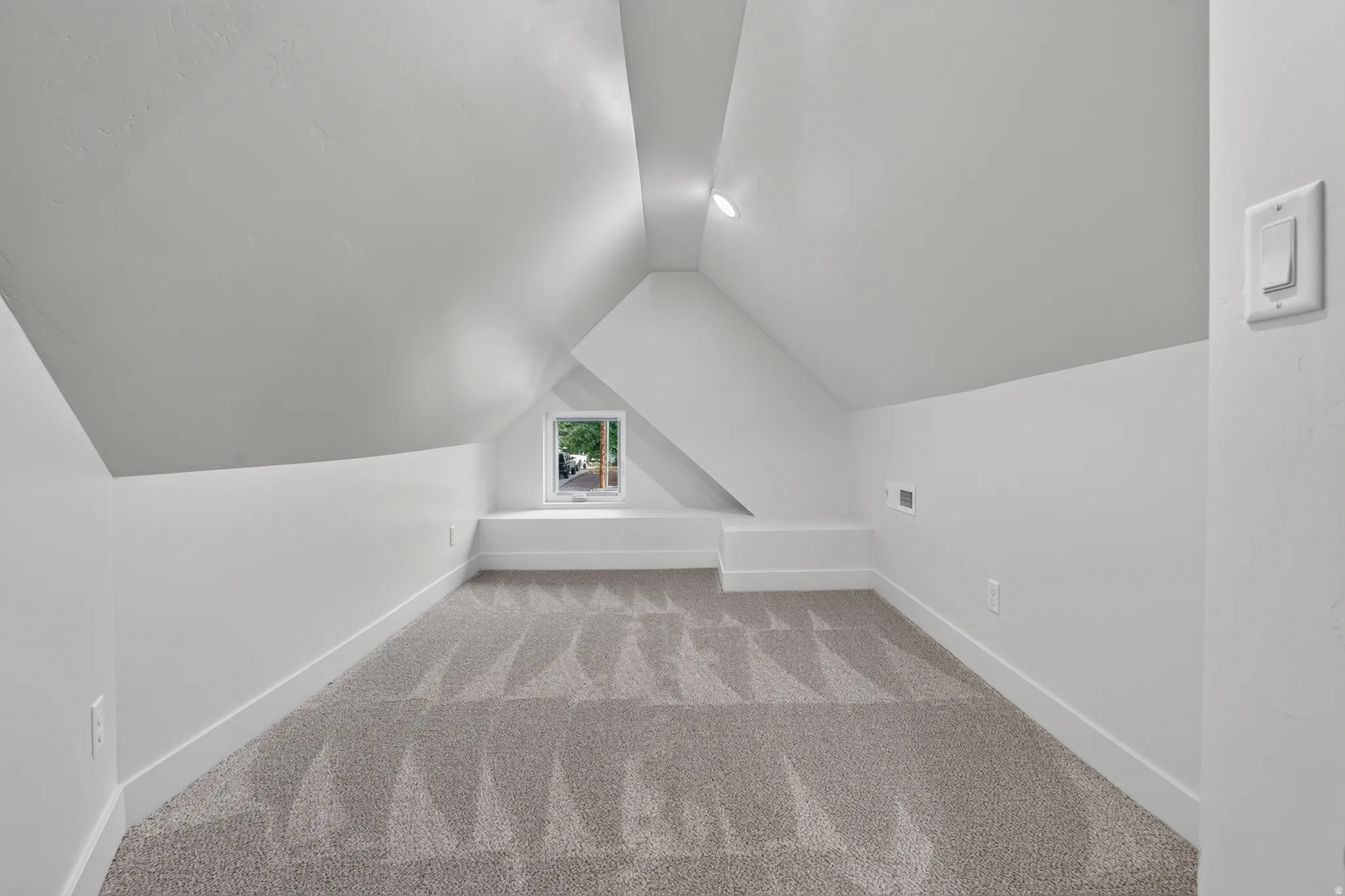 Attic space with sloped ceilings, recessed lighting, a single window, and grey patterned carpeting