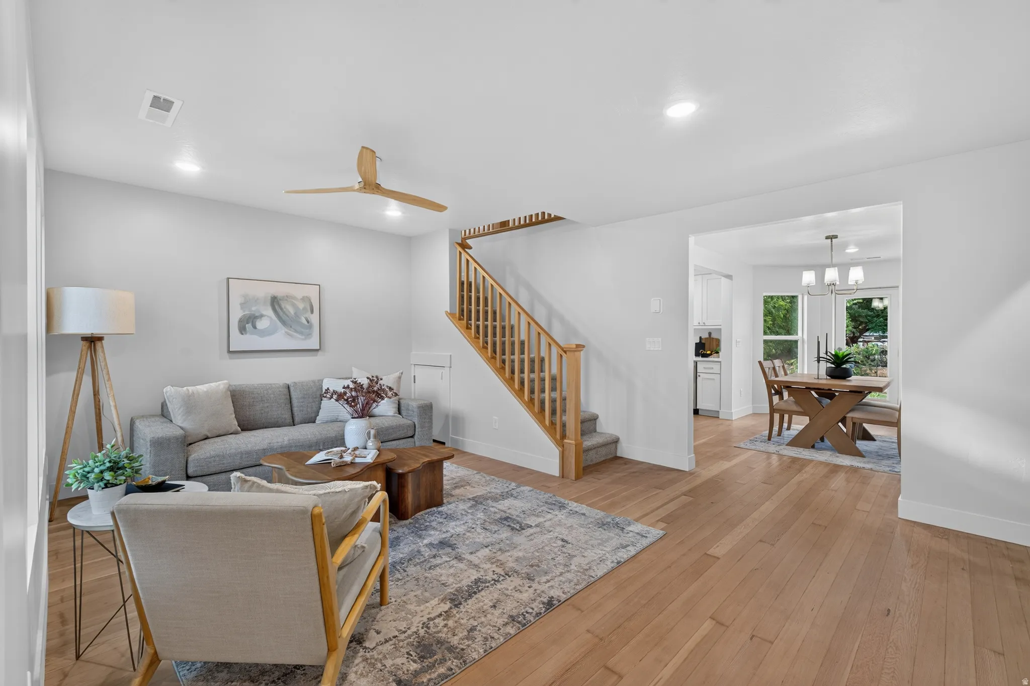 Hardwood flooring, recessed lighting, ceiling fan, natural wood staircase with carpeted treads, and a dining area with a chandelier
