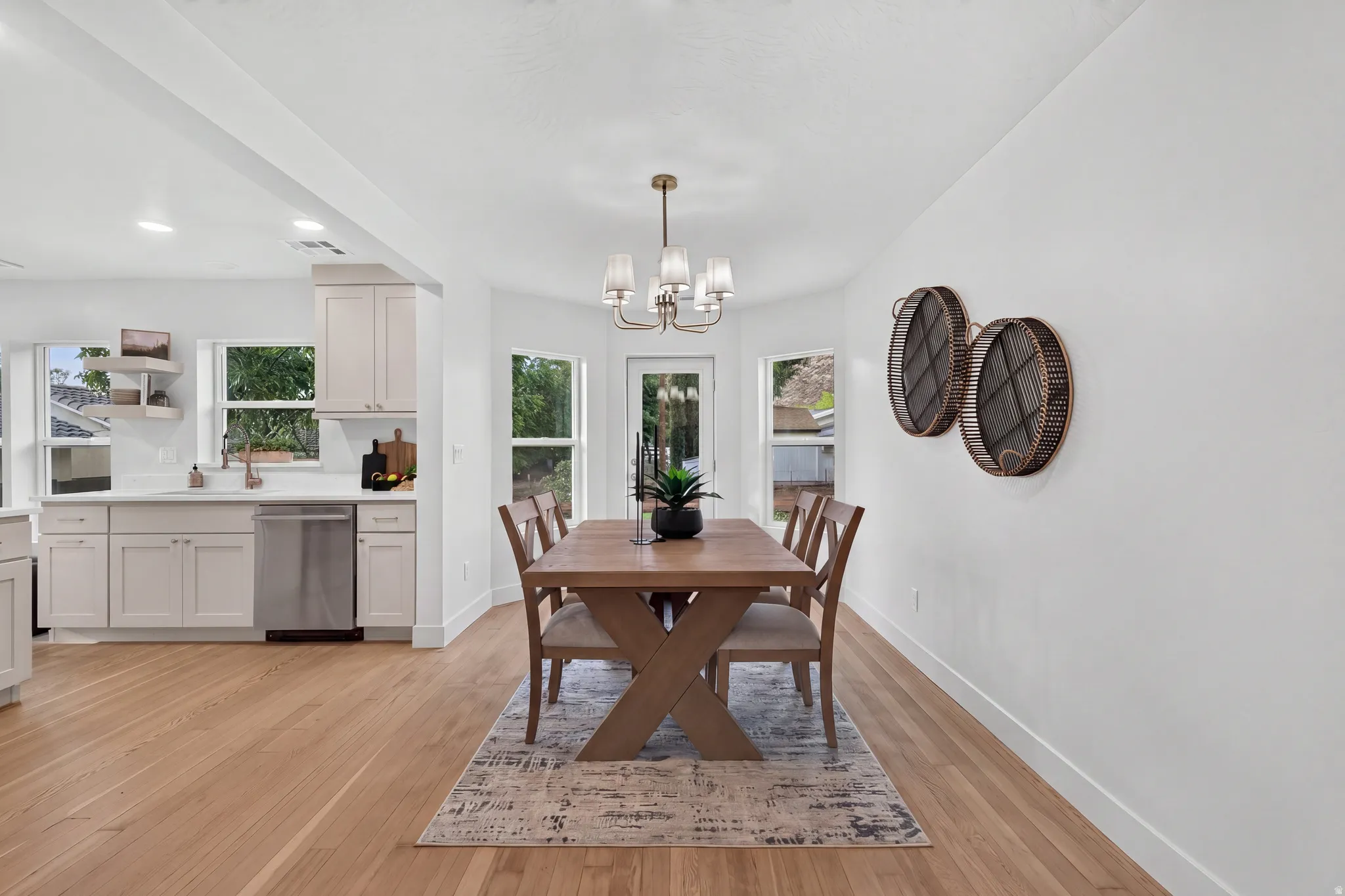 Hardwood-style flooring throughout, kitchen featuring white cabinetry and stainless steel dishwasher, white countertops, and a dining area with a chandelier