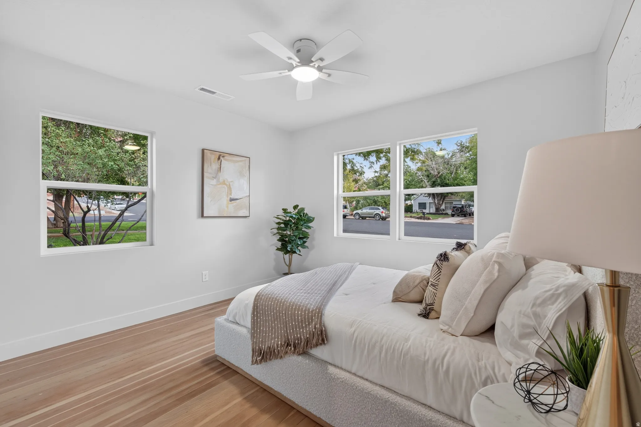 Wood-finish flooring, multiple windows, ceiling fan, and crisp white walls