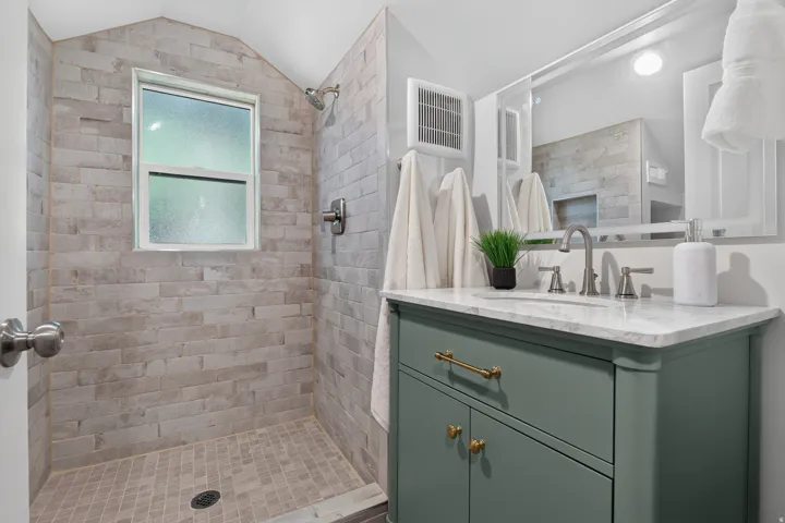 Tiled shower with a window, single vanity with a stone countertop, under-mount sink, and a framed mirror