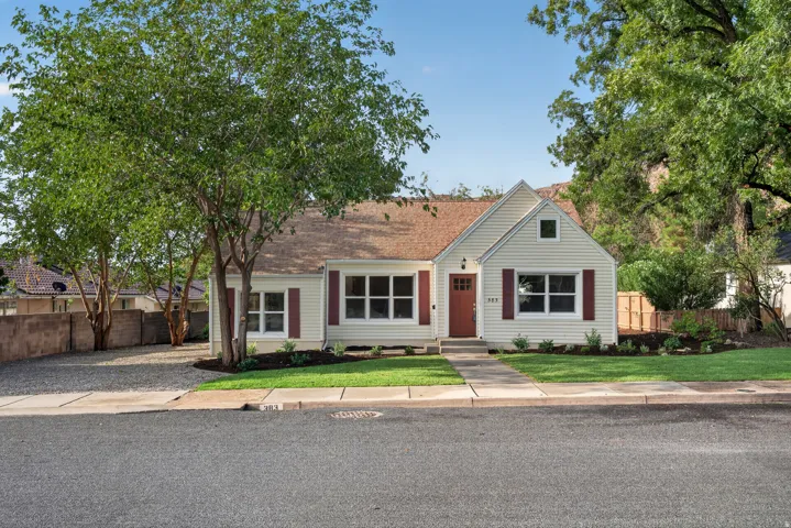 White siding exterior with a red front door, red shutters, front yard landscaping, and mature trees