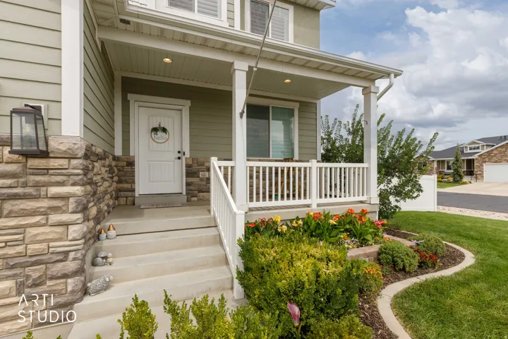 Covered front porch with white railings, stone veneer accents, concrete steps, and a landscaped garden bed
