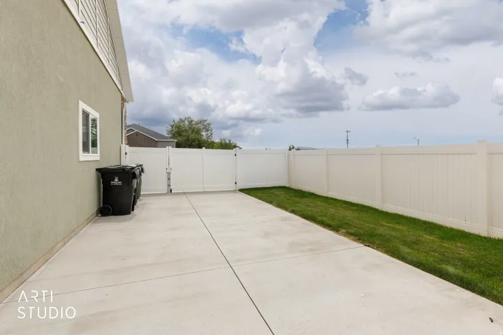 Concrete patio with a privacy fence, an access gate, and a grass strip