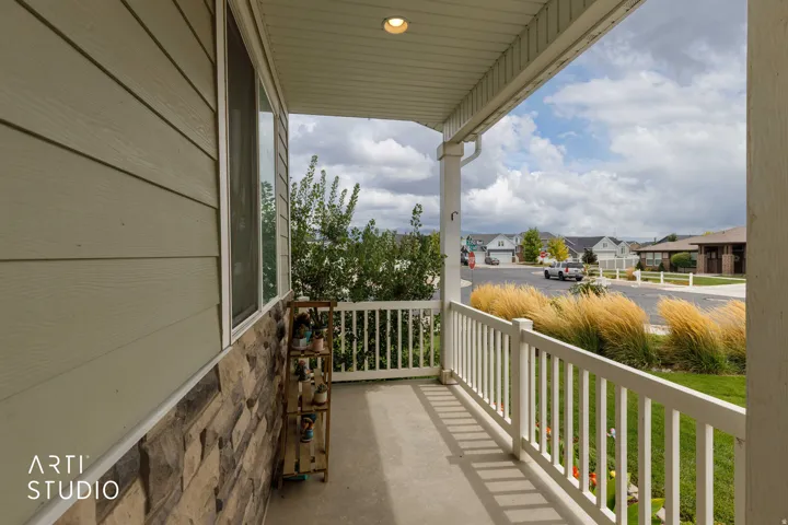 Covered front porch featuring a concrete surface, white railing, and exterior lighting