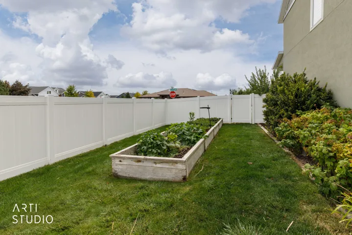 Expansive lawn area featuring a raised garden bed, mature shrubs, and a white privacy fence with an access gate