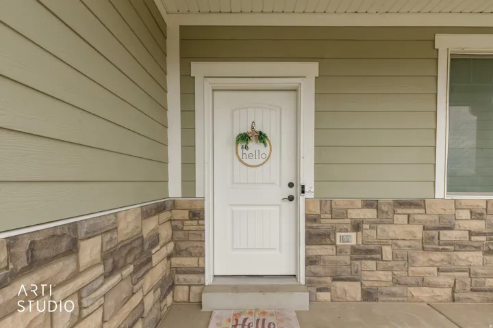 Entry door with decorative glass insert, flanked by stone veneer and horizontal siding, with a concrete porch