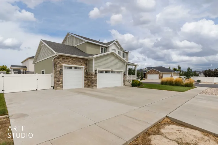 Two-story residence featuring a stone and siding exterior, dual garage doors, a wide concrete driveway, and a white privacy fence