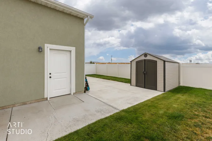 Exterior stucco finish, white trim door, outdoor wall sconce, concrete path, detached storage shed, and vinyl fencing