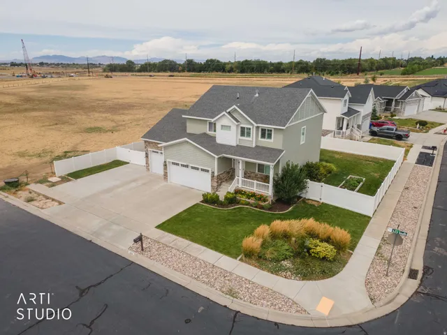 Two-story residence featuring light green siding and stone accents, a multi-car garage, manicured lawn, and a white picket fence enclosing the property