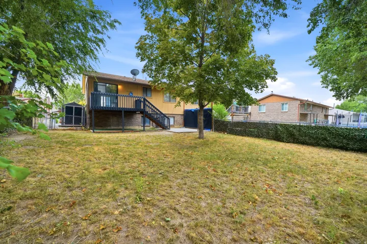 Expansive backyard with mature shade trees and level lawn, complemented by a yellow exterior with elevated deck and stair access