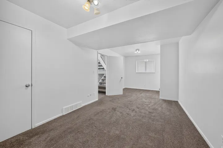 Expansive carpeted area with white walls, track lighting, and a window with blinds