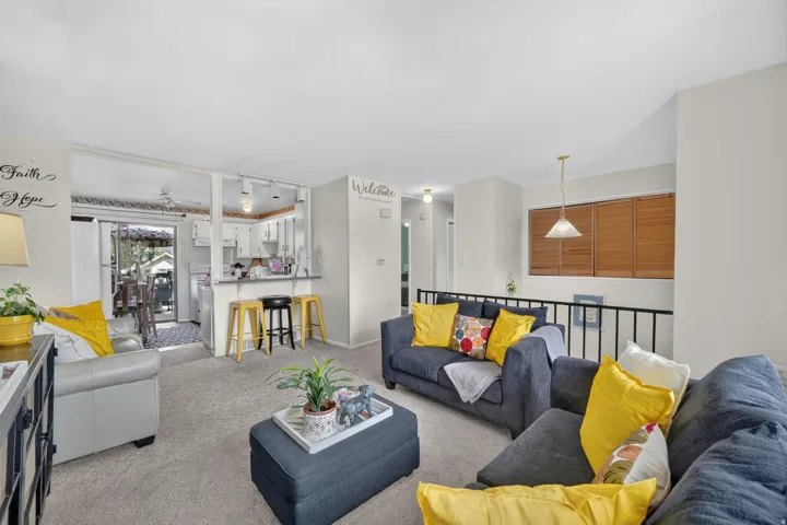 Carpeted living area with a partial wall separating a kitchen with white cabinetry and a breakfast bar