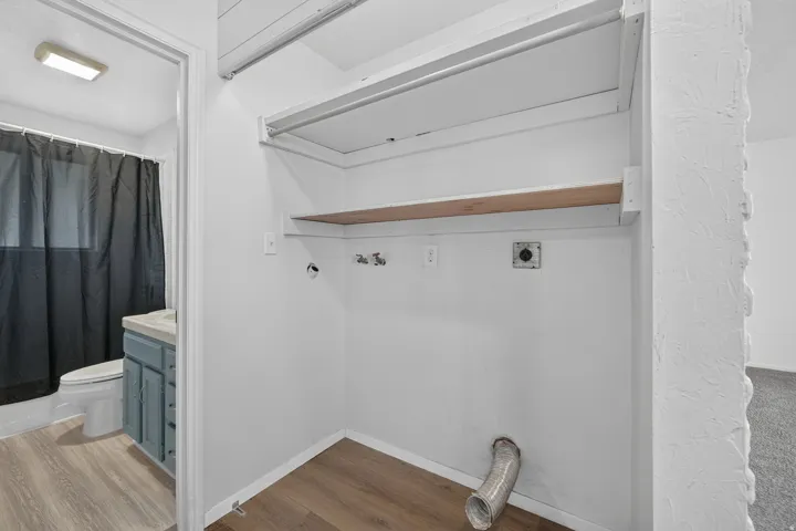 Spacious walk-in closet featuring white subway tile surround, wood-finish shelving, wall-mounted fixtures, and wood-finish flooring