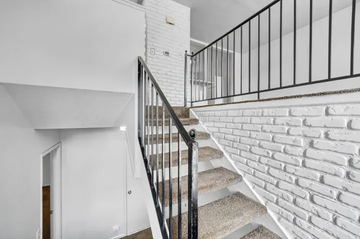 Staircase featuring carpeted treads, white brick-finish wall, and black metal railings