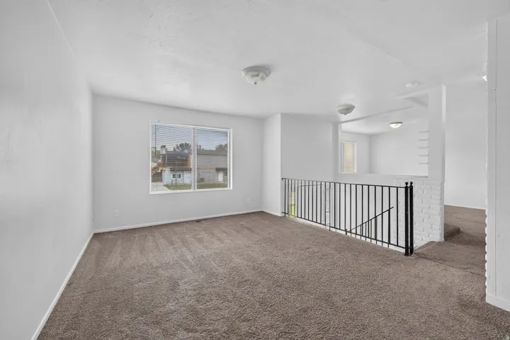 Open concept space with neutral carpeting, white walls, a large window, and a black metal railing