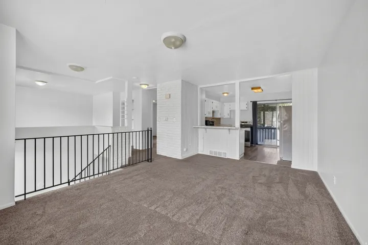 Open-concept living area with carpet flooring, a white painted brick accent wall, and recessed lighting