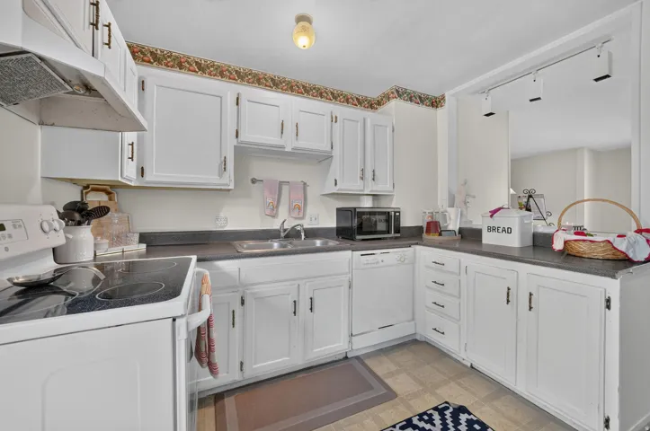 Bright kitchen featuring crisp white cabinetry with ample storage, dark countertops, and stainless steel appliances including a range and refrigerator