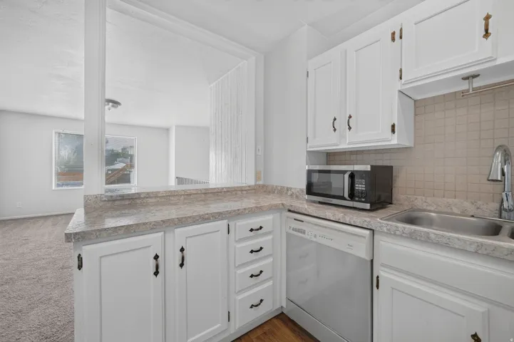 Kitchen featuring white cabinetry, a double basin stainless steel sink, a tile backsplash, and wood-finish flooring