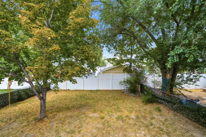 Lawn area featuring mature trees and a white privacy fence