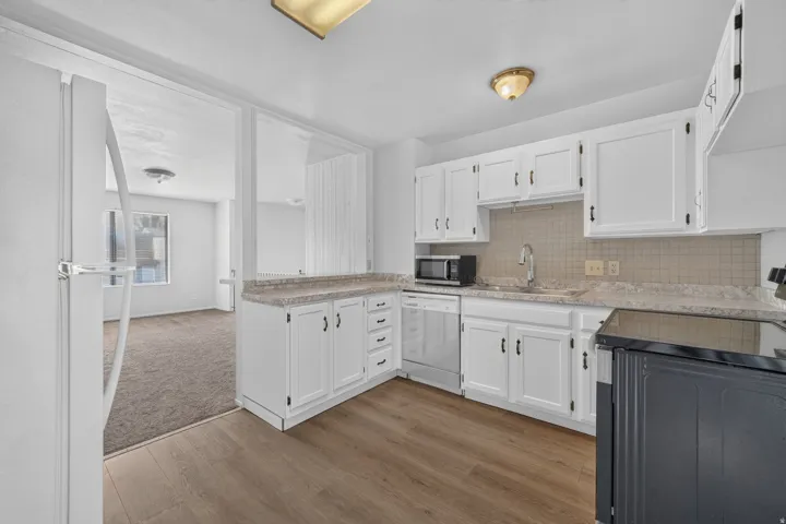White cabinetry, wood-finish flooring, light-toned countertops, and a tile backsplash