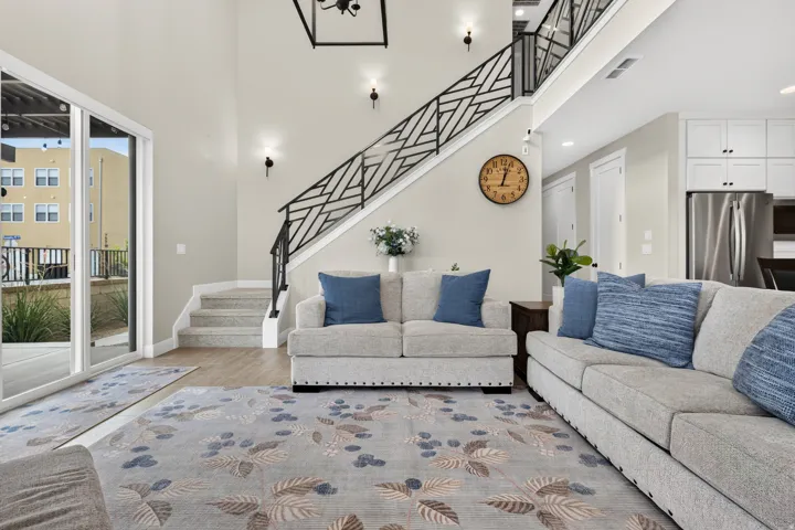 Two-story living area with high ceilings, contemporary open-concept staircase with decorative metal railing, wood-finish flooring, and recessed lighting
