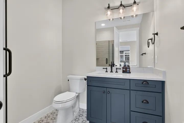 Navy blue vanity with a white countertop, patterned floor tiling, and a three-light fixture