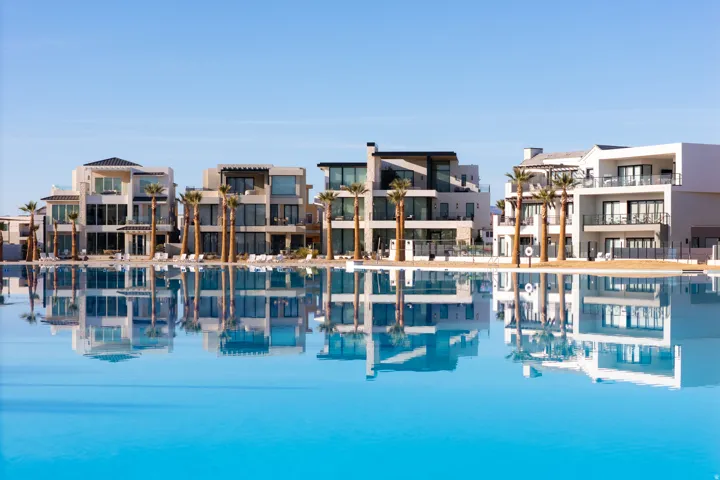 Expansive water feature with a wide perimeter, multiple balconies with dark railings, and a row of palm trees