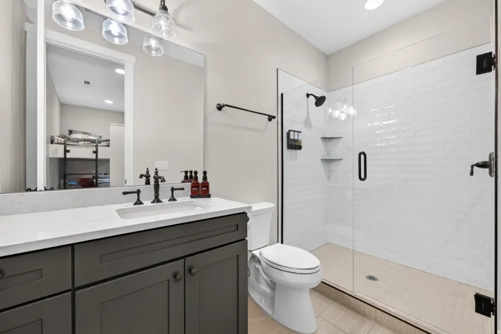 Modern bathroom featuring a single vanity with a white countertop and dark cabinetry, a glass-enclosed shower with white subway tile, and a dark-finish shower system