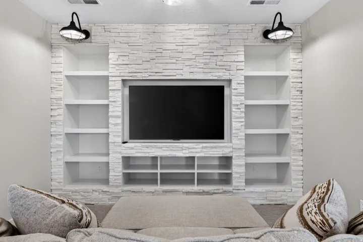 Stone veneer accent wall with integrated media console, built-in shelving, and dual industrial-style sconces