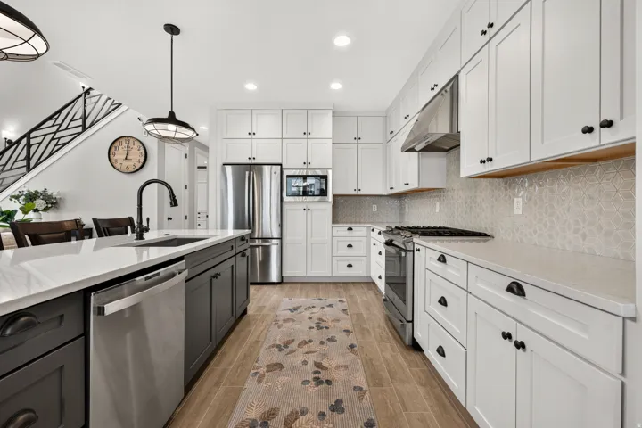 Kitchen featuring a central island with a sink, stainless steel appliances, white shaker cabinetry, patterned backsplash, and wood-finish flooring