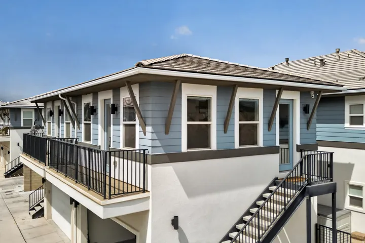 Exterior featuring light blue horizontal siding, white trim, a dark tile roof, a private balcony with black metal railing, and an exterior staircase with black metal railing
