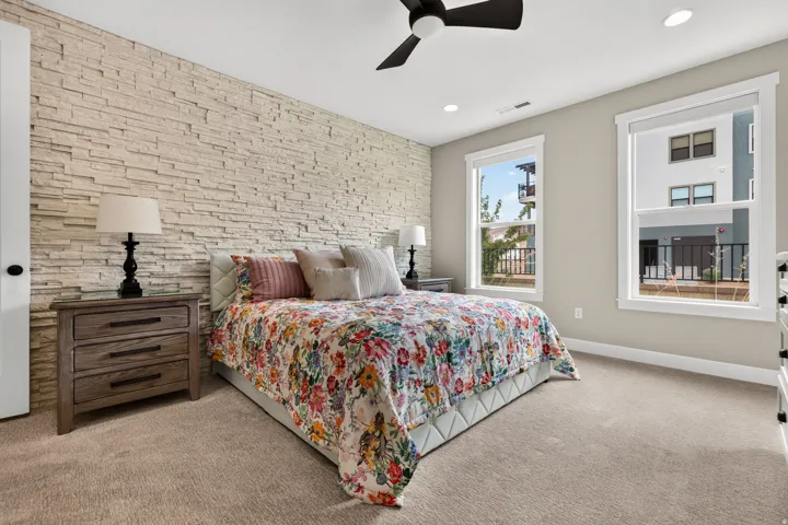 Textured accent wall, ceiling fan, recessed lighting, two windows with white trim, and carpeted flooring